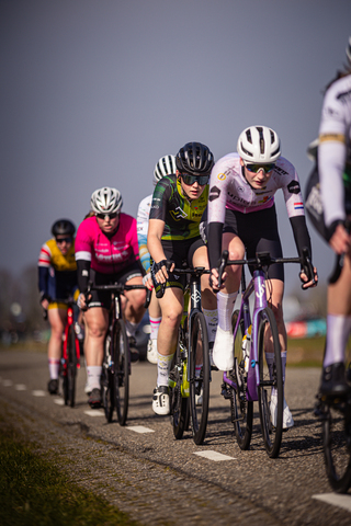 A group of cyclists riding on a road, one woman in the lead is wearing number 13.