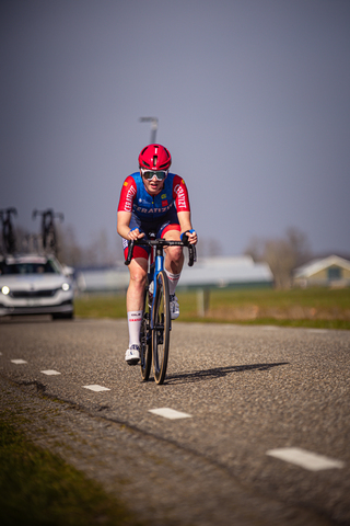 A young male cyclist in a race with his helmet reflecting the sun, racing down road number 1 of Drentse 8 van Westerveld.