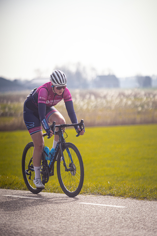 A woman with a pink jersey is riding her bicycle on a road.