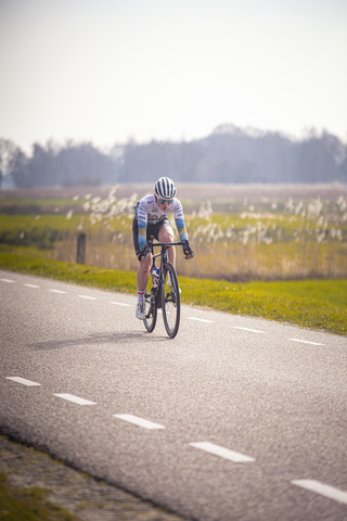 A cyclist wearing a blue and white shirt is riding on a road.