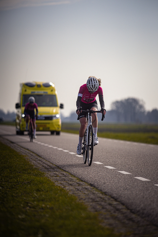 A woman riding a bicycle past another cyclist and a yellow bus.