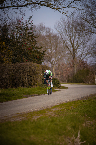 A person riding a bicycle down a road. The cyclist is wearing a green and white jersey and a white helmet.