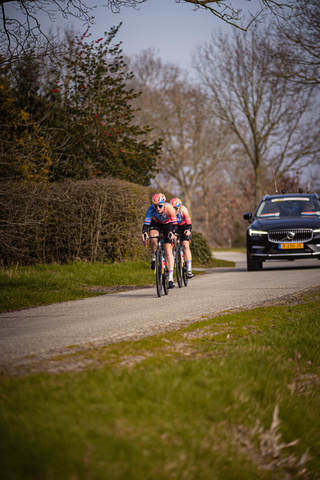 Two cyclists are racing on the road, they are wearing numbers 5 and 7.