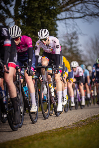 A cyclist wearing a white jersey with the word "Giant" written on it leads a group of cyclists in a race.