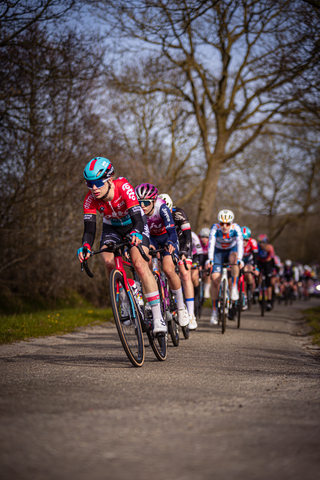 A man and woman race their bikes on a road. The man is wearing a red jersey with the number 27 on it.