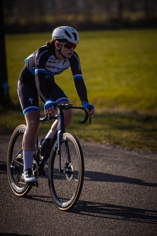 Woman wearing a black and blue jersey riding a bicycle down the road.