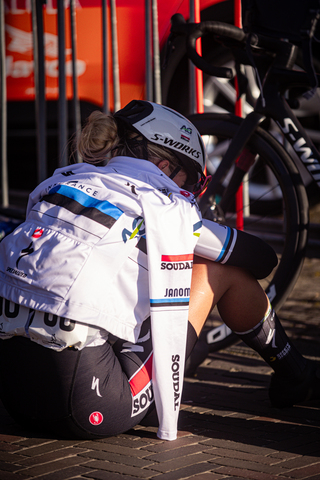 A woman wearing a jacket with the word Soord printed on it. She is looking down at her bike.