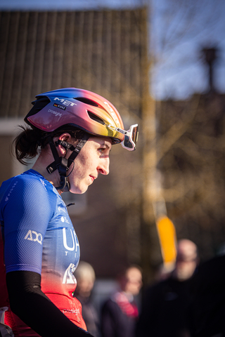 A cyclist in a blue jersey and a red helmet is wearing an UCI Wielrennen pin.