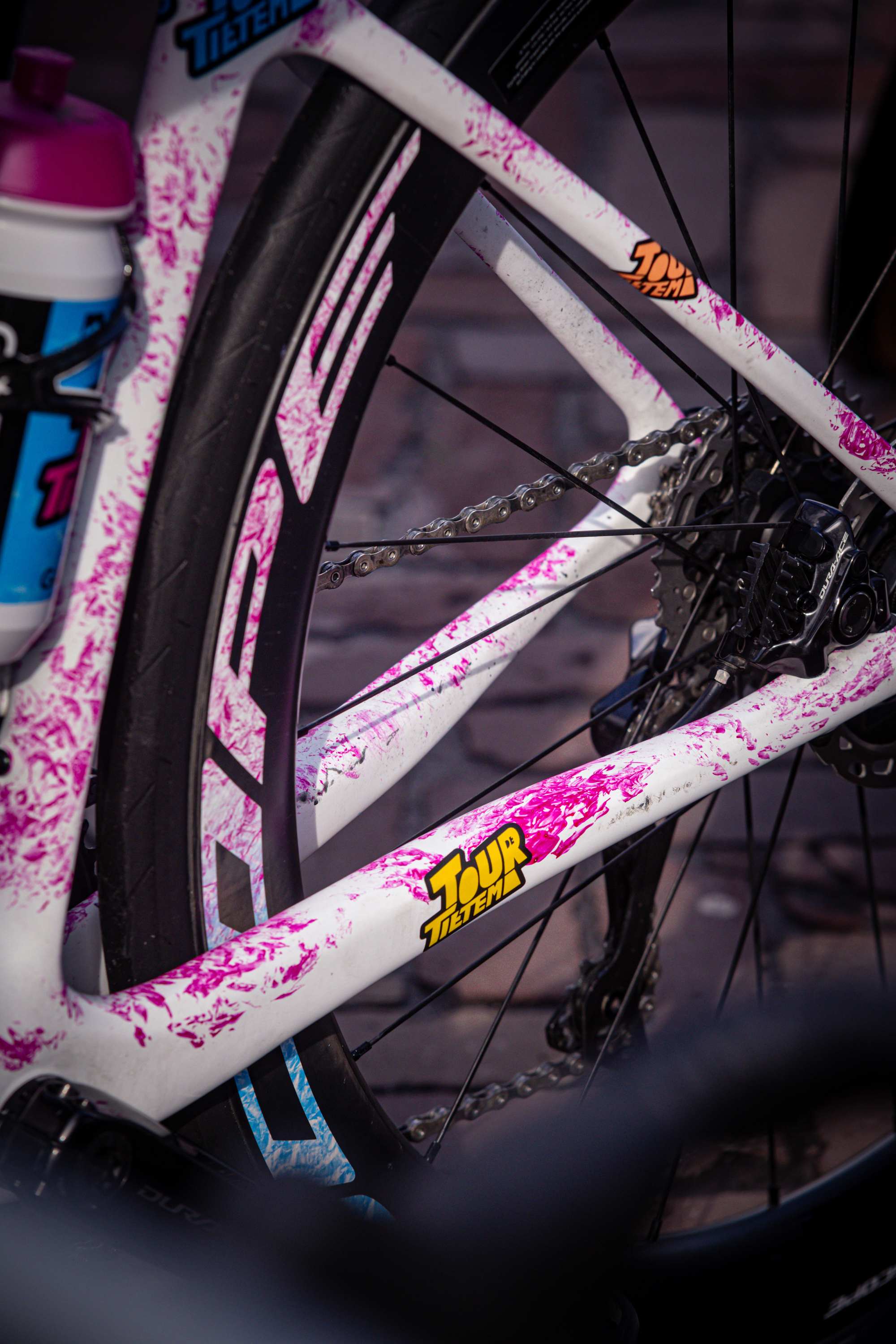 A pink and white bicycle that is being sponsored by Giant, with a blue water bottle sitting on top of it.