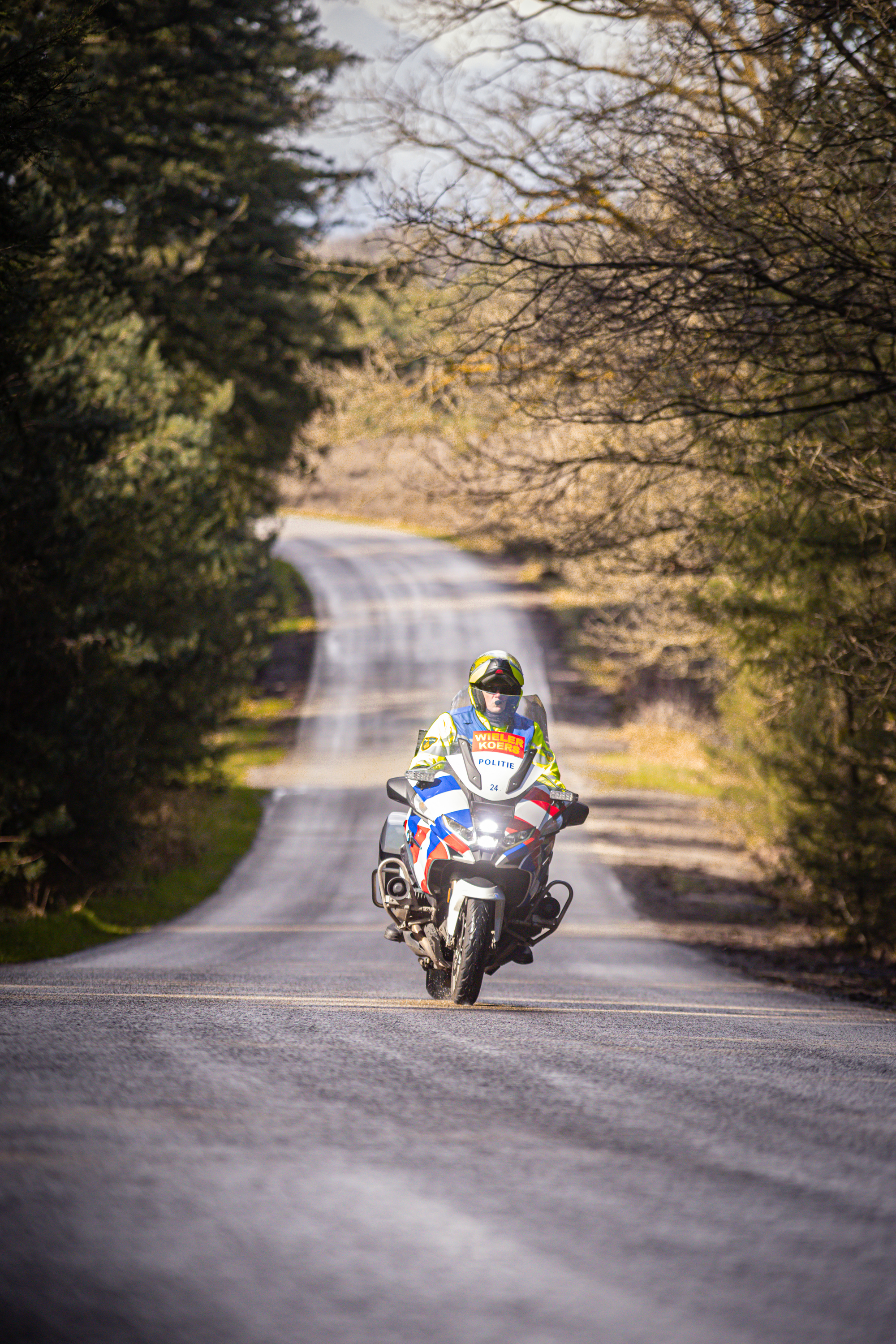 A cyclist wearing a yellow helmet with red and blue markings rides down the road.