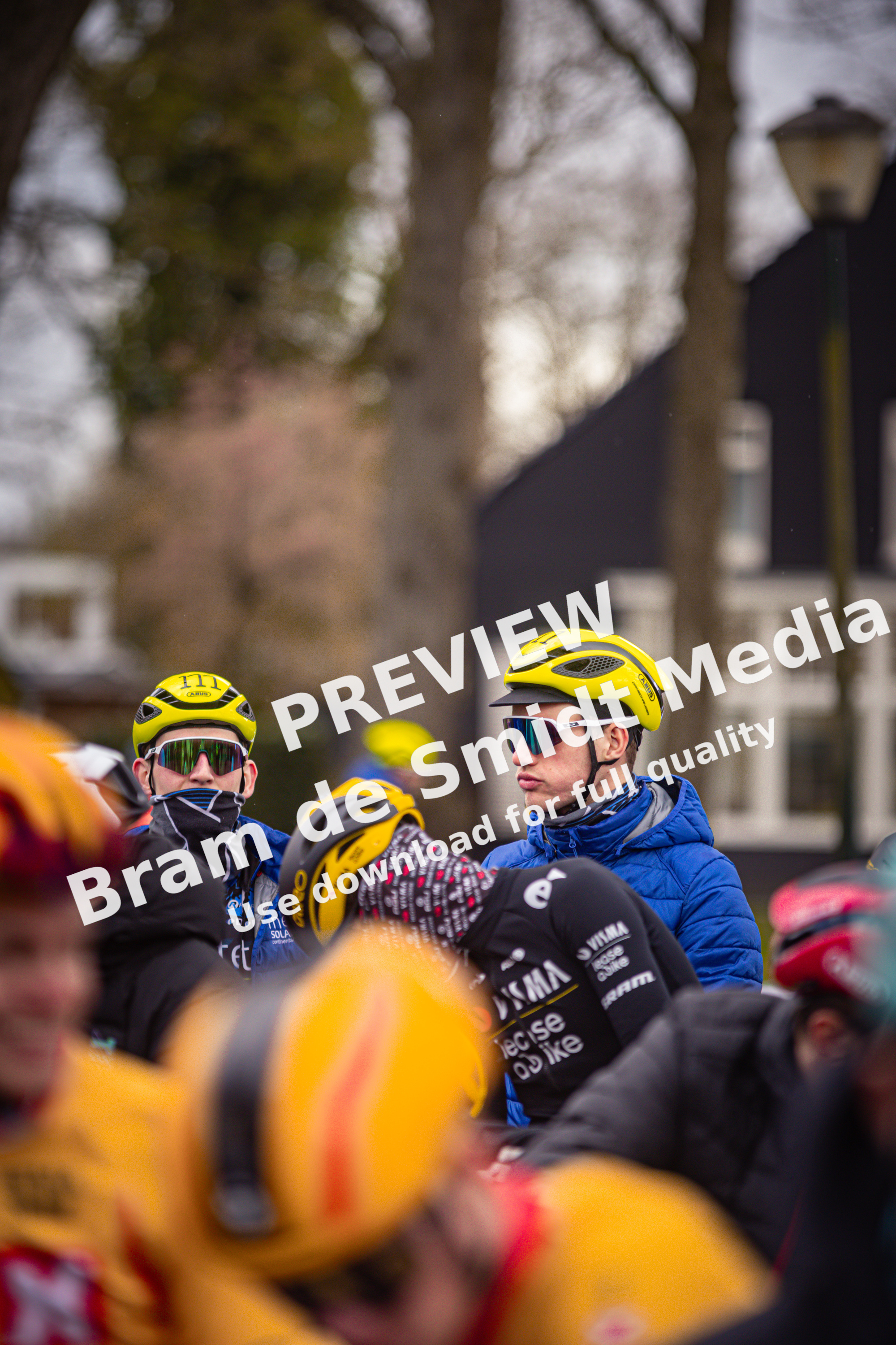 A group of cyclists in yellow and blue, one is wearing a Wielrennen helmet.