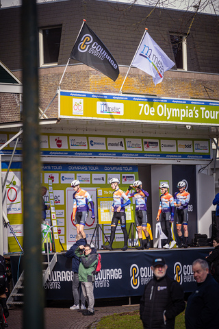 A group of cyclists pose for a photo in front of an Olympic banner.