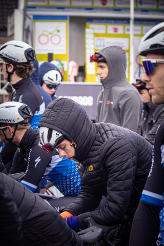 A group of cyclists wearing Wielrennen gear are gathered around a sign.