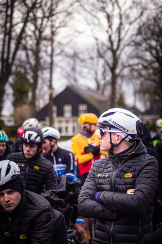 A group of cyclists are preparing for a race, one of them is wearing a black jacket with the number 17 on it.