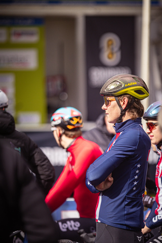 A cyclist wears a helmet adorned with a yellow bike symbol. He stands behind two other cyclists, all of them wearing helmets.