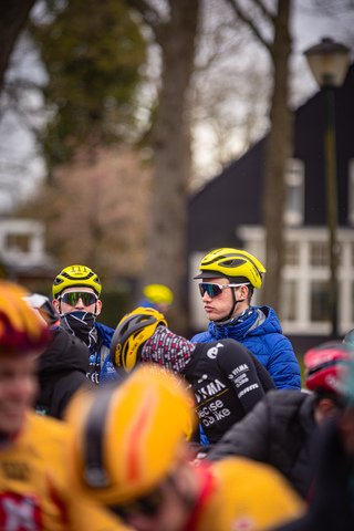 A group of cyclists in yellow and blue, one is wearing a Wielrennen helmet.