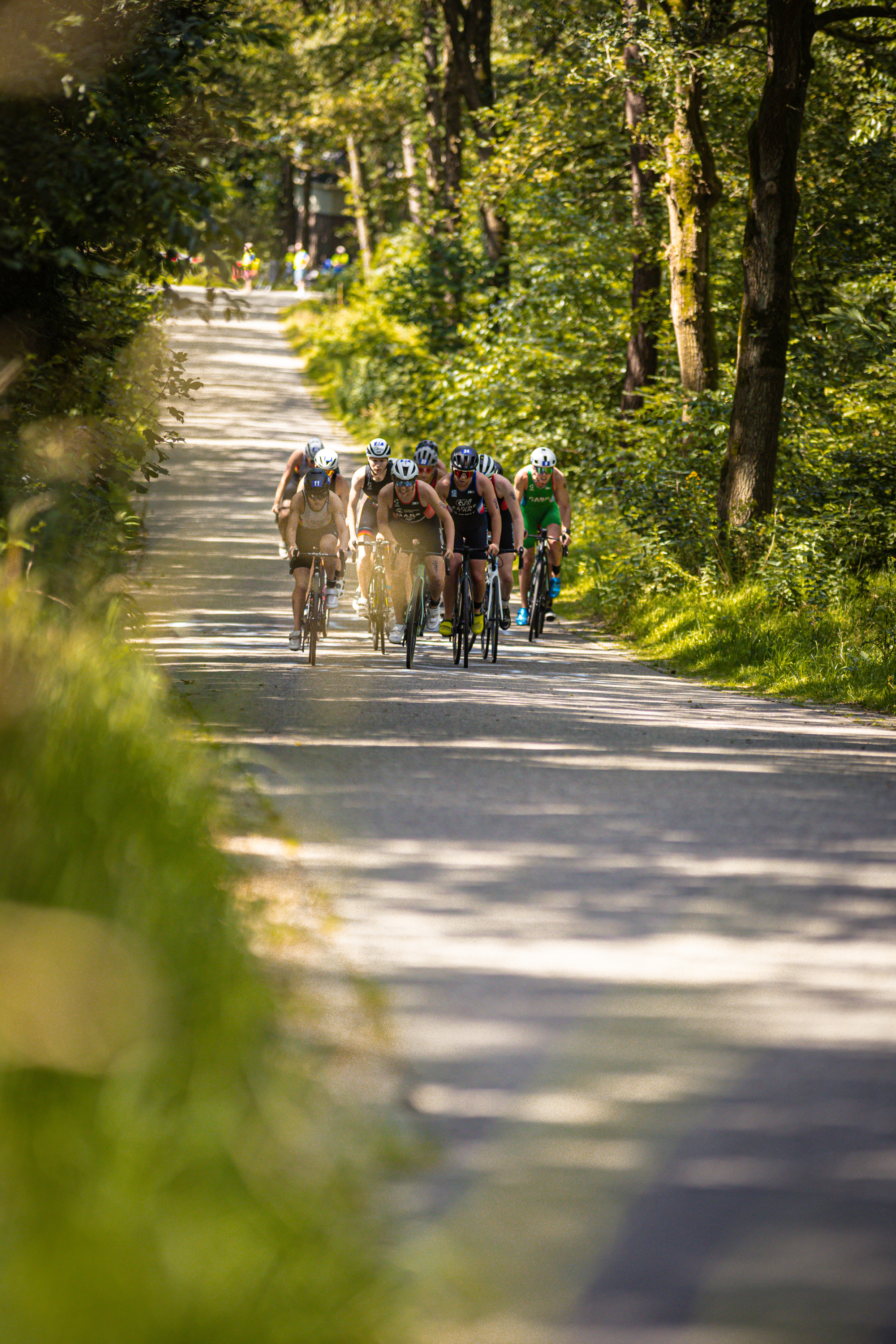 A group of triathletes are riding bikes in a line down the street.