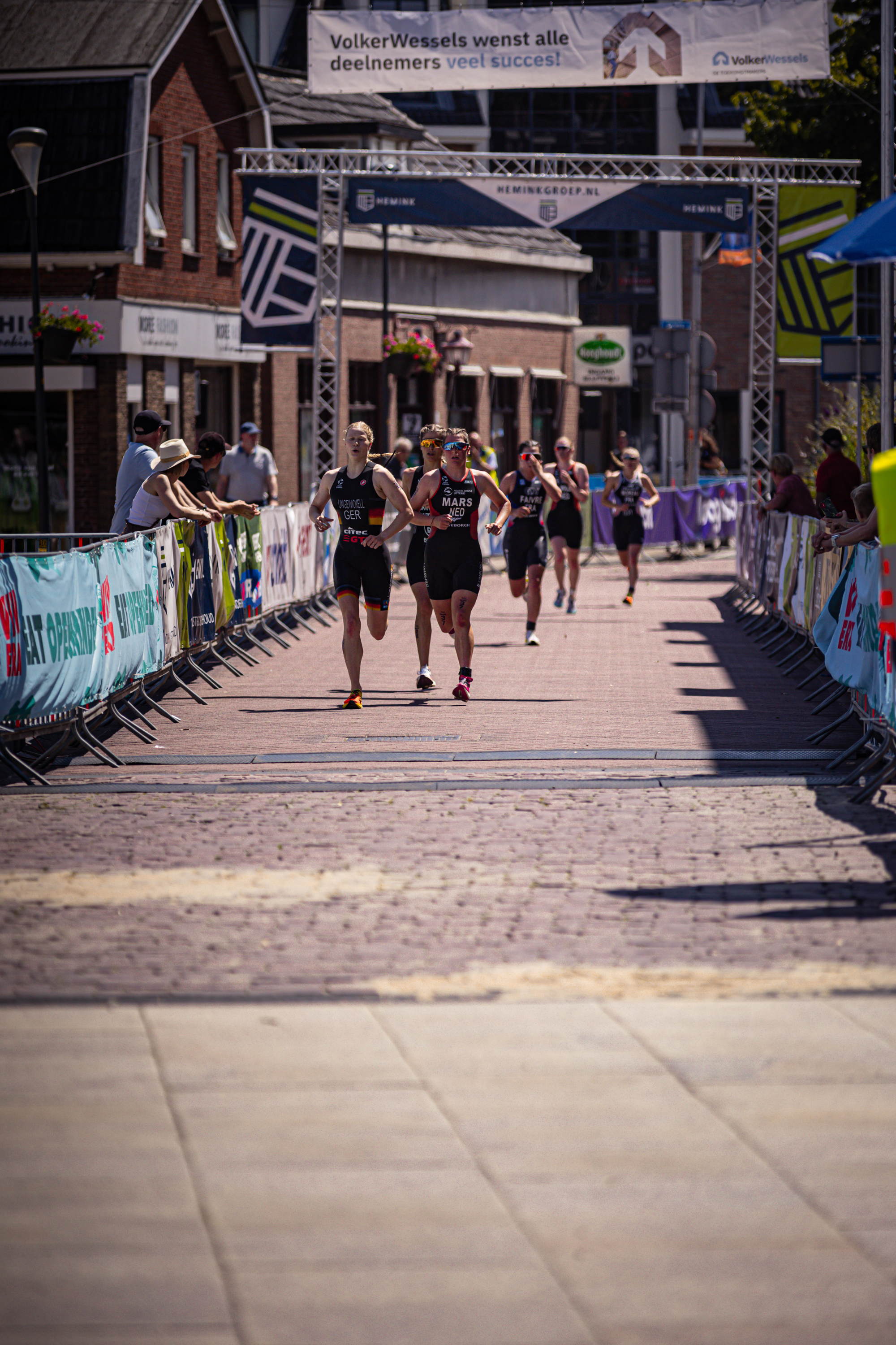 A group of women are running a marathon on a street lined with banners for Elite Triathlon.