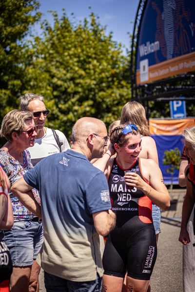 A woman is wearing a blue headband and an Elite Triathlon Unit shirt, standing near a group of people.