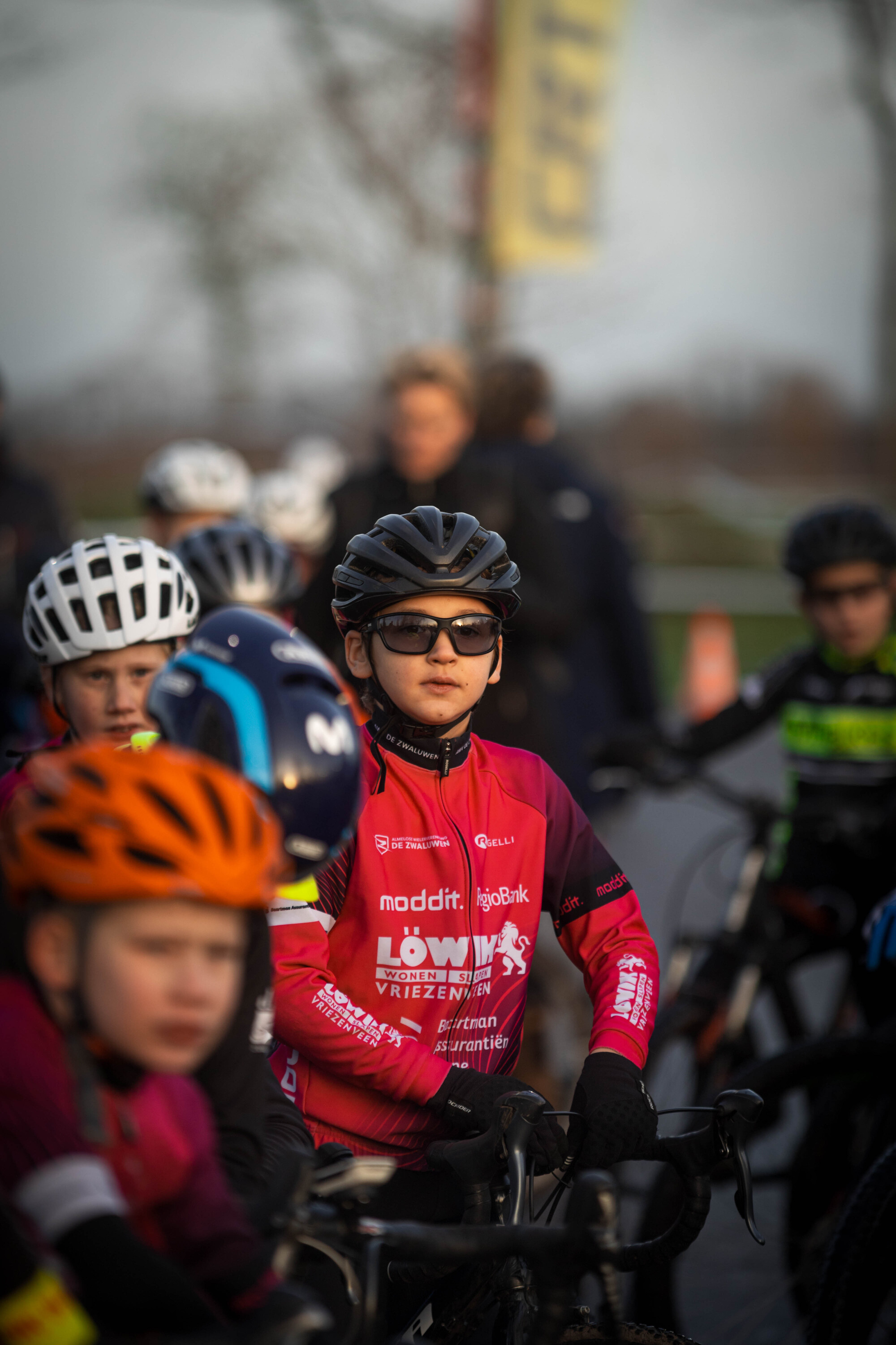 A group of young cyclists wearing colorful jerseys for a Jeug cyclocross event sponsored by GOW.