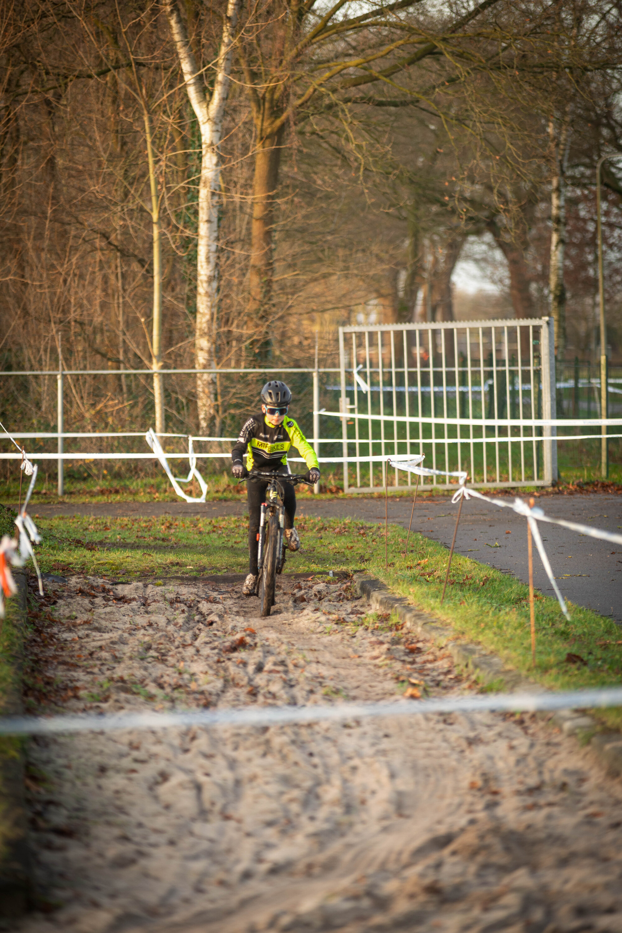 A boy is riding a bicycle in an area with bare trees and grass on the ground.