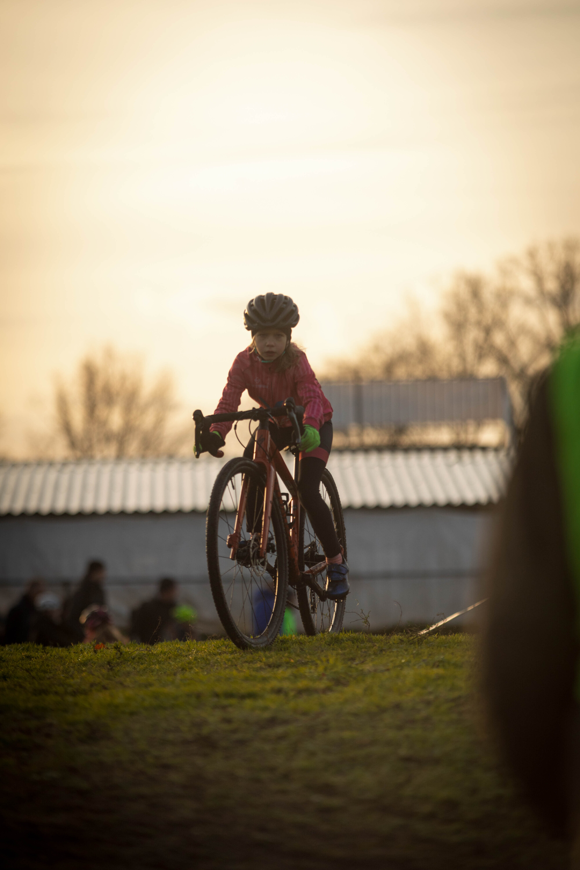 A girl rides her bike through a grassy field during sunset.