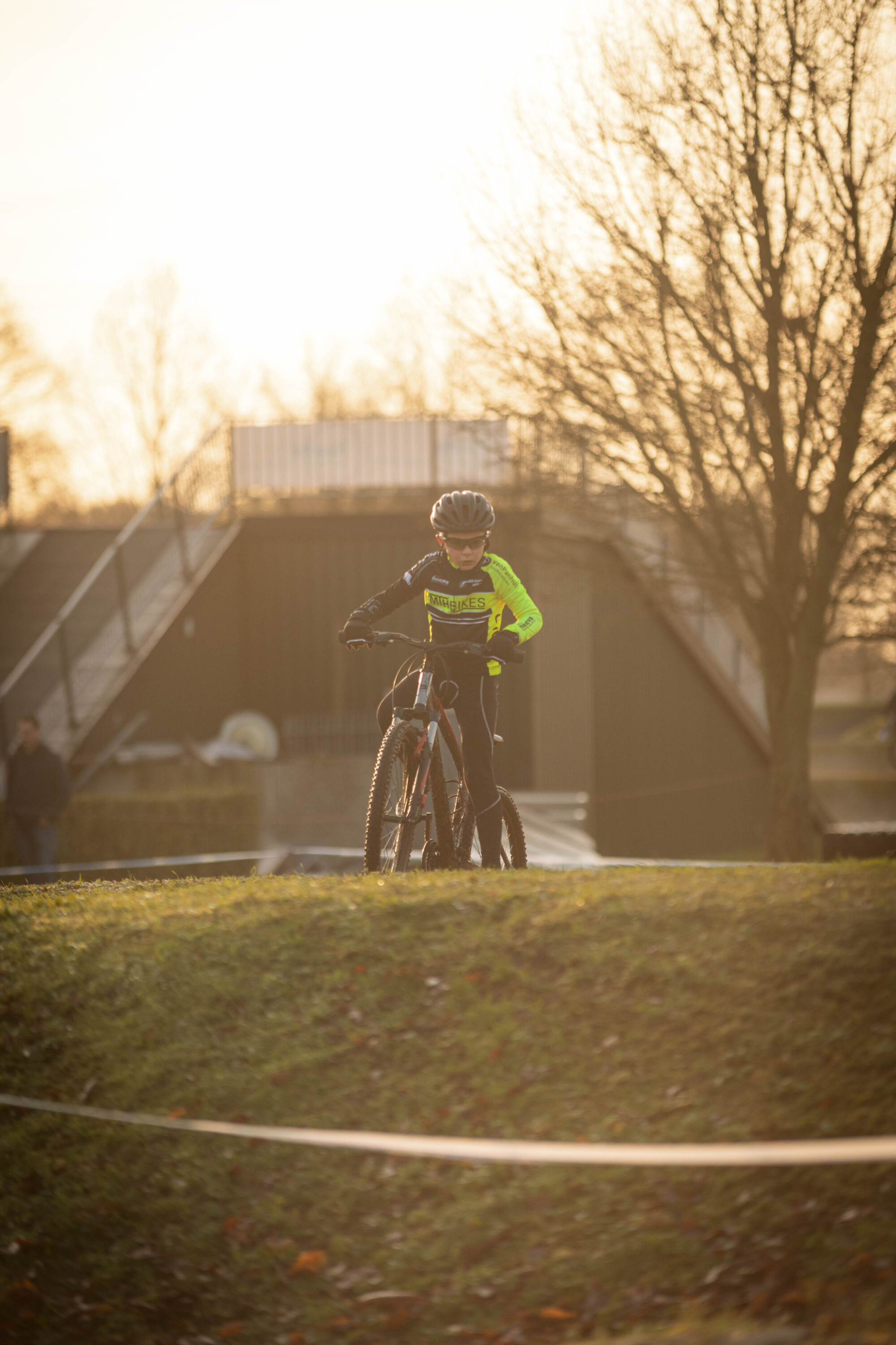 A young person wearing a neon green shirt and black helmet is riding their bike.