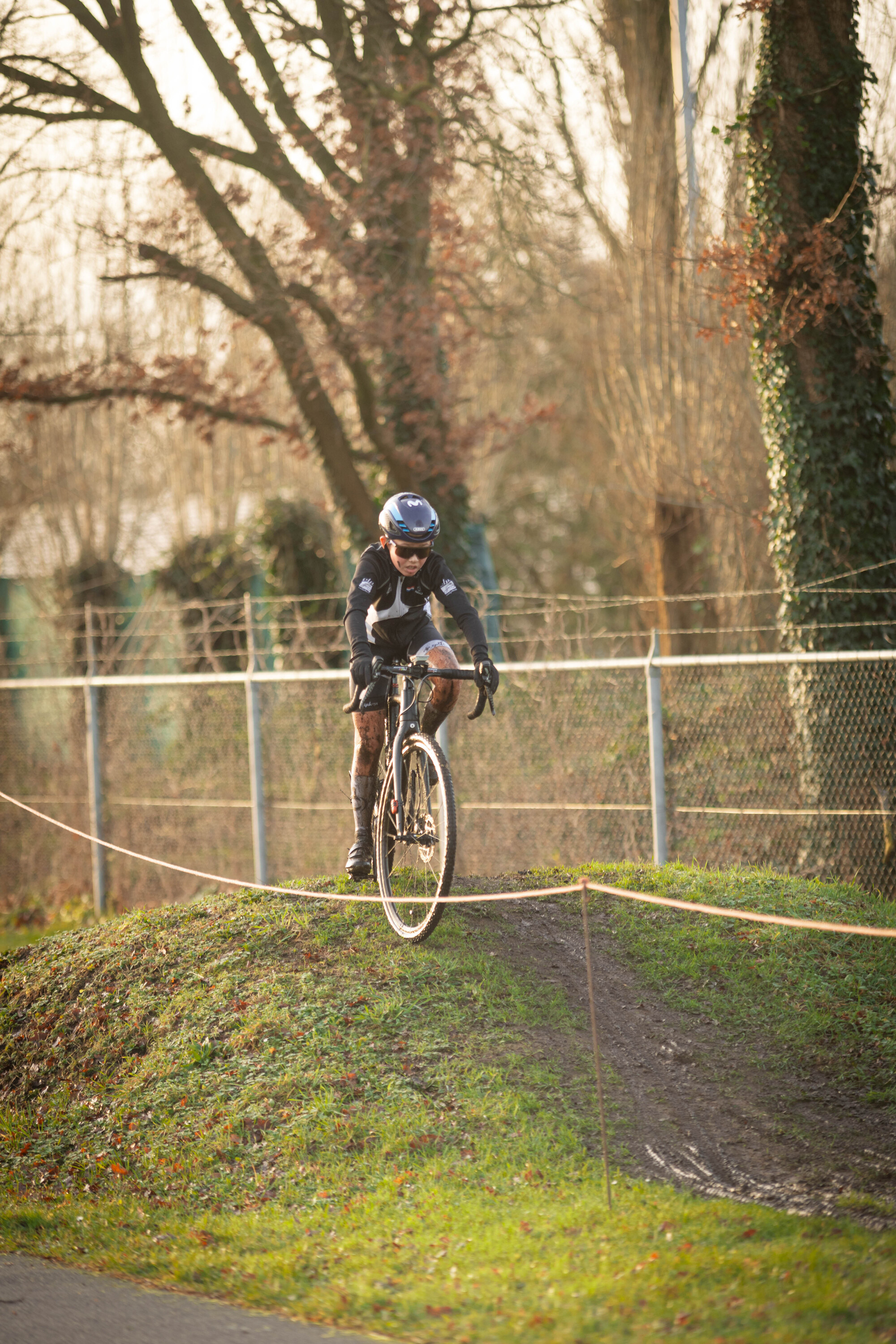 A person on a bicycle wearing a blue helmet is riding along a grassy area next to a fence.