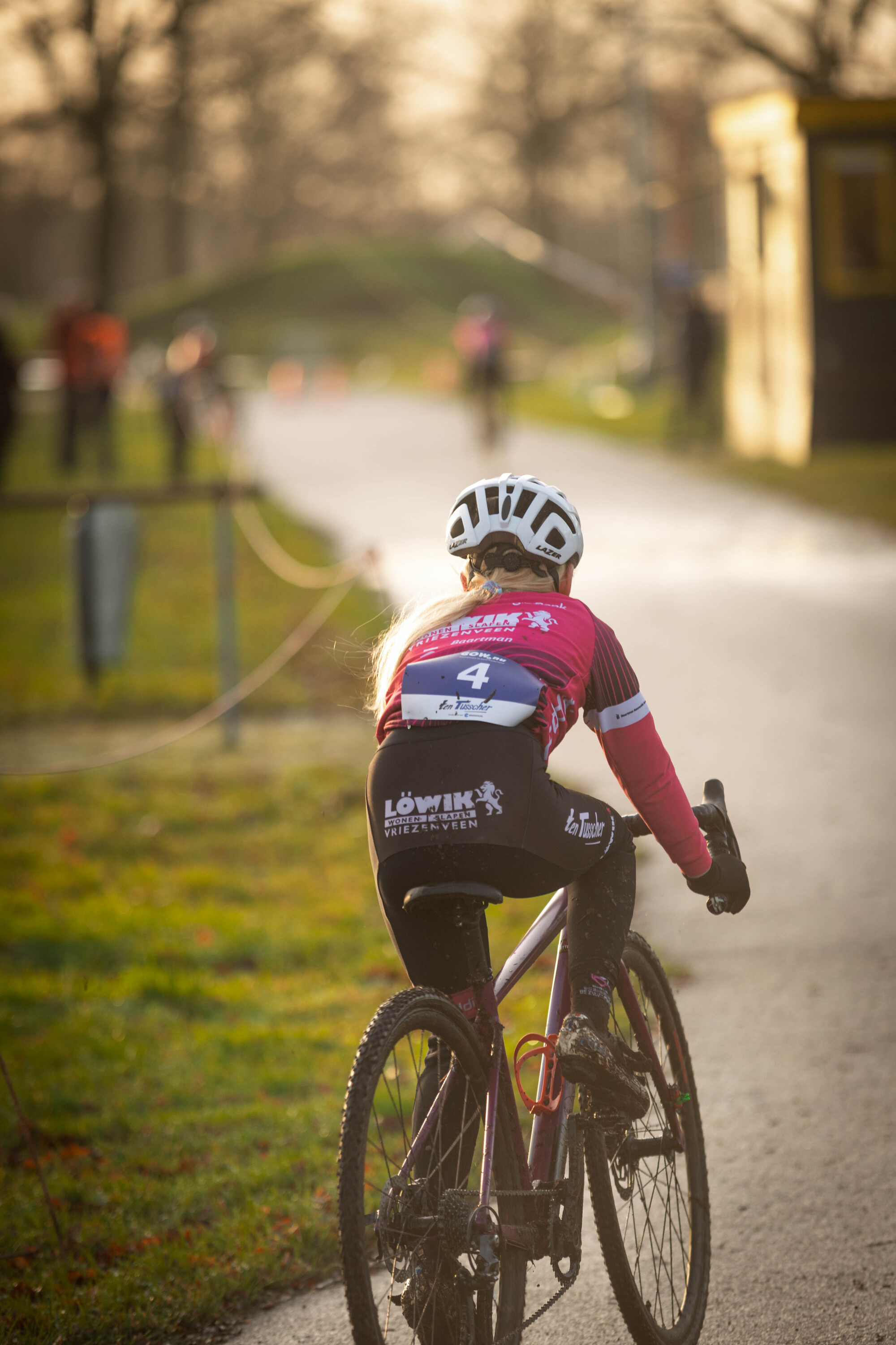 A cyclist wearing a pink jersey with the words Jeugd 1 + 2 on it rides along a road.