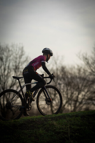 A person on a bike in front of trees, the cyclist is wearing a helmet and a pink shirt.