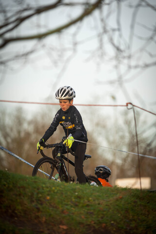 A young cyclist wearing a black and yellow outfit riding his bike down a grassy hill.