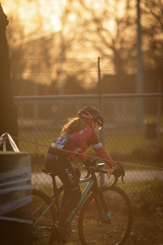 A girl wearing a pink shirt and helmet rides her bicycle in the dark.