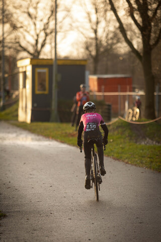 A young person in a black and pink outfit rides a bike.