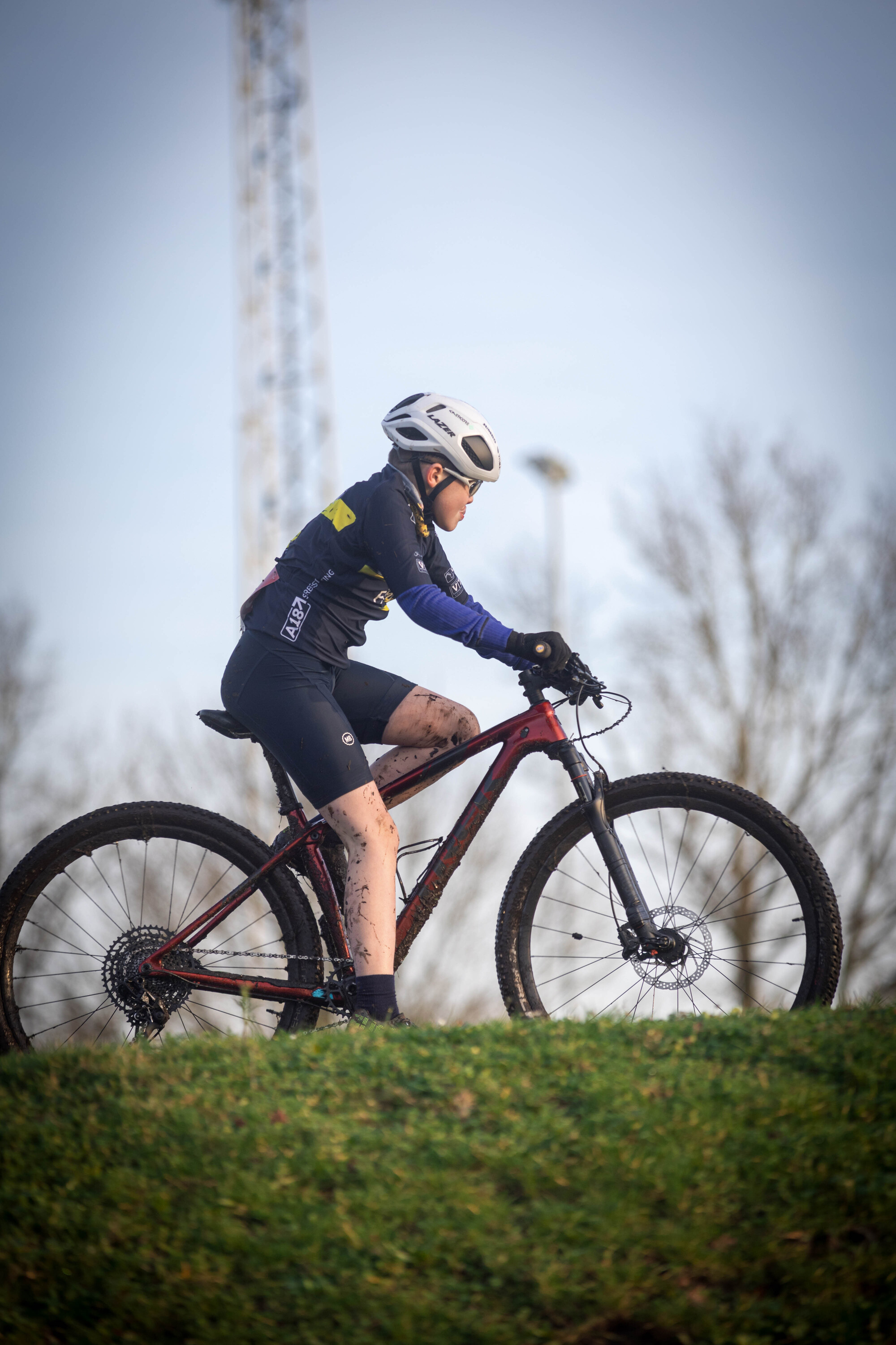 A cyclist in a black helmet is riding a red bike on a grassy hill.