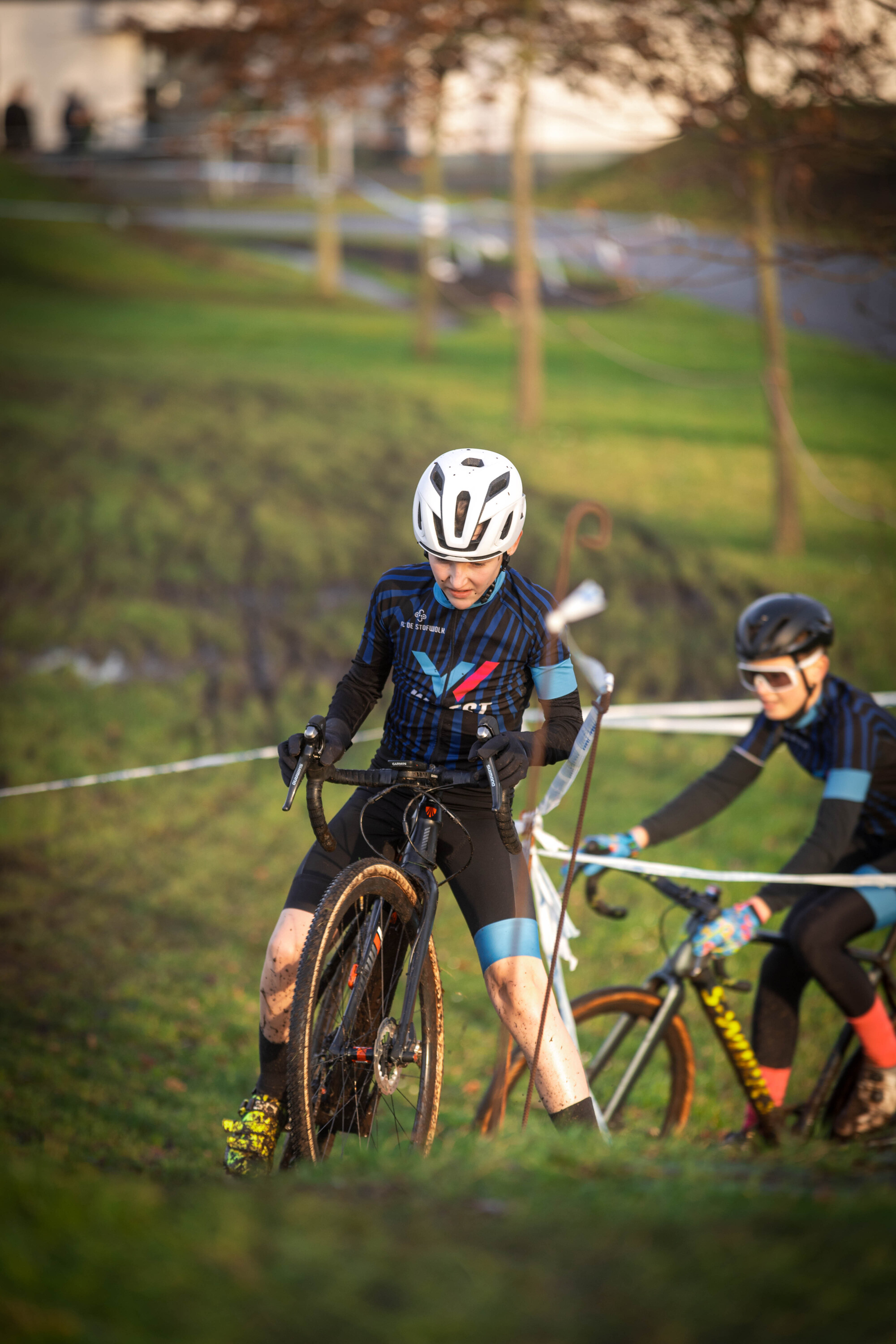 A boy and a girl are getting ready for a cyclocross race on a grassy hill.