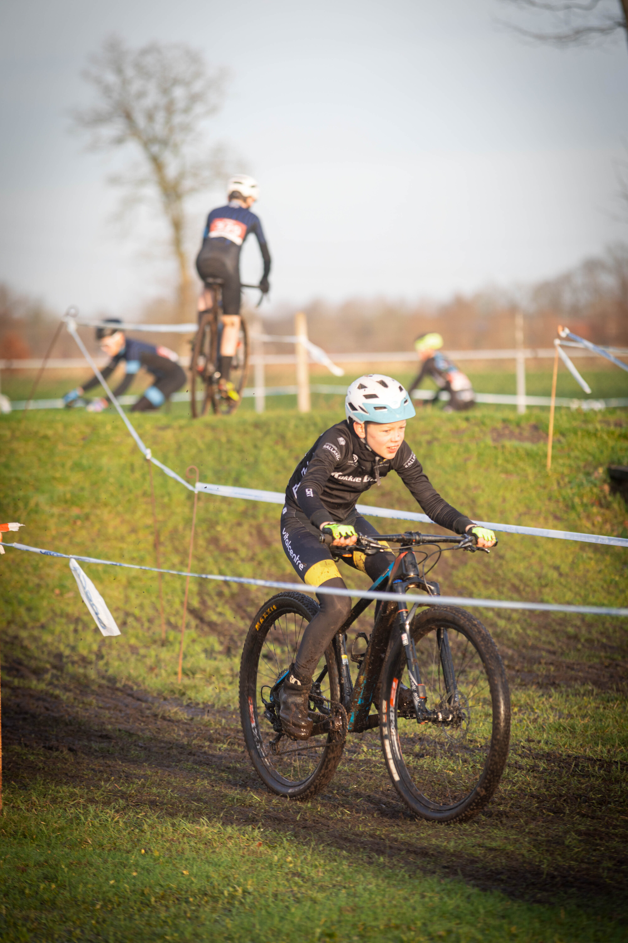 A young woman is wearing a blue helmet and riding a black bike in a cyclocross race.