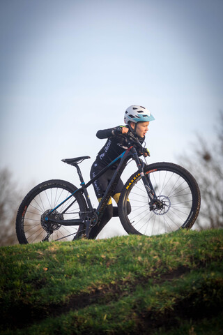 A young cyclist wears a blue helmet while riding a black and blue mountain bike.