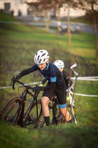 Two young men are playing a game of cyclocross, one of them is wearing an orange helmet.