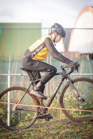 A young man wearing a yellow and black shirt rides his bicycle.