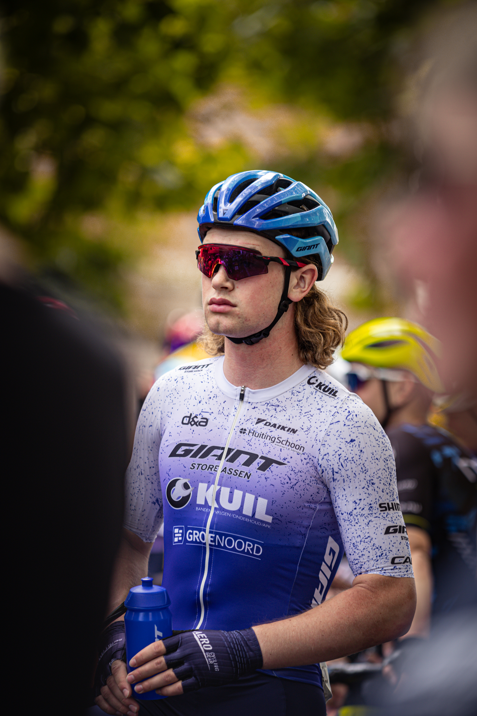 A cyclist at the Midden Brabant Poort Omloop race holds a blue bottle.