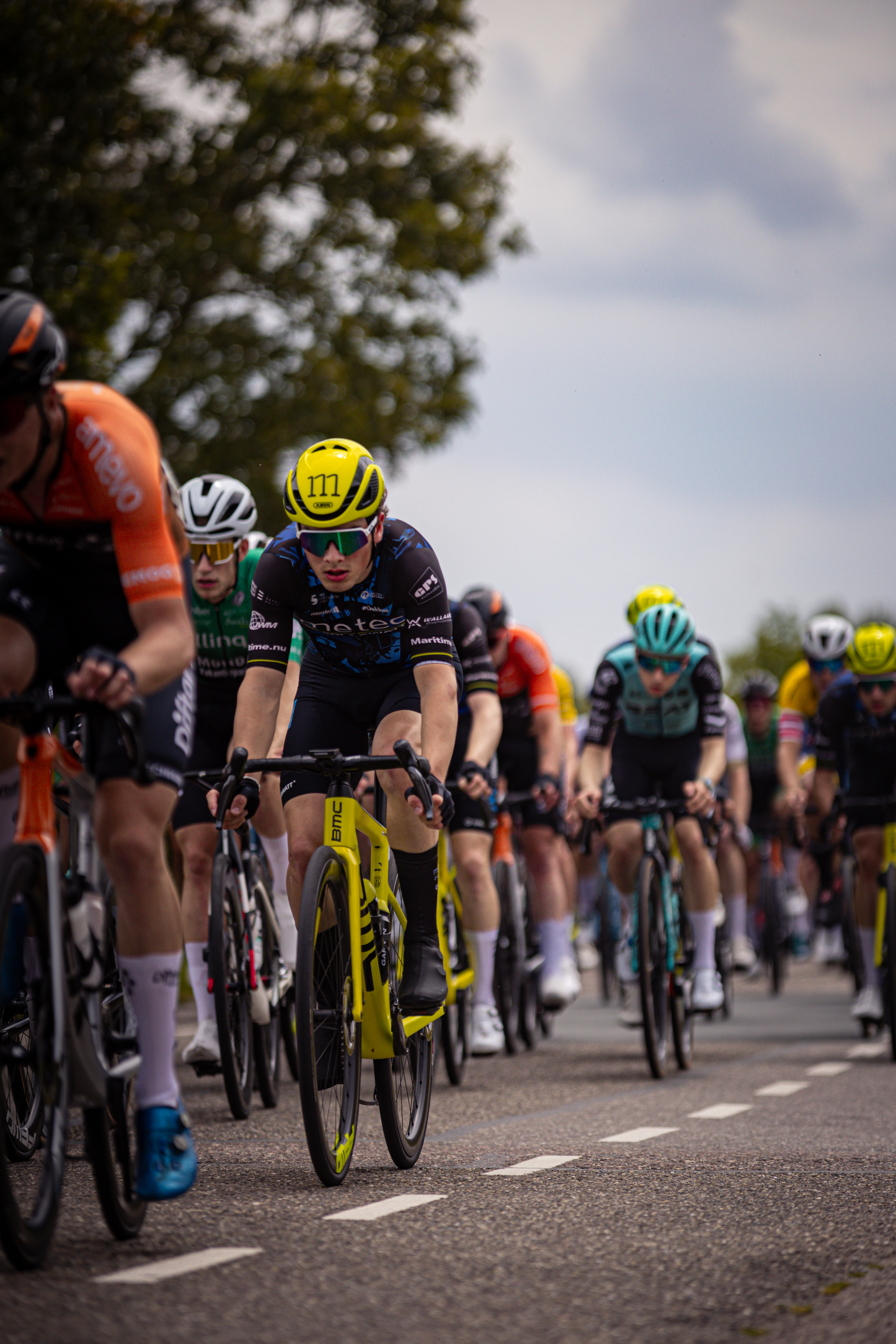 A group of cyclists riding on a road in front of trees.