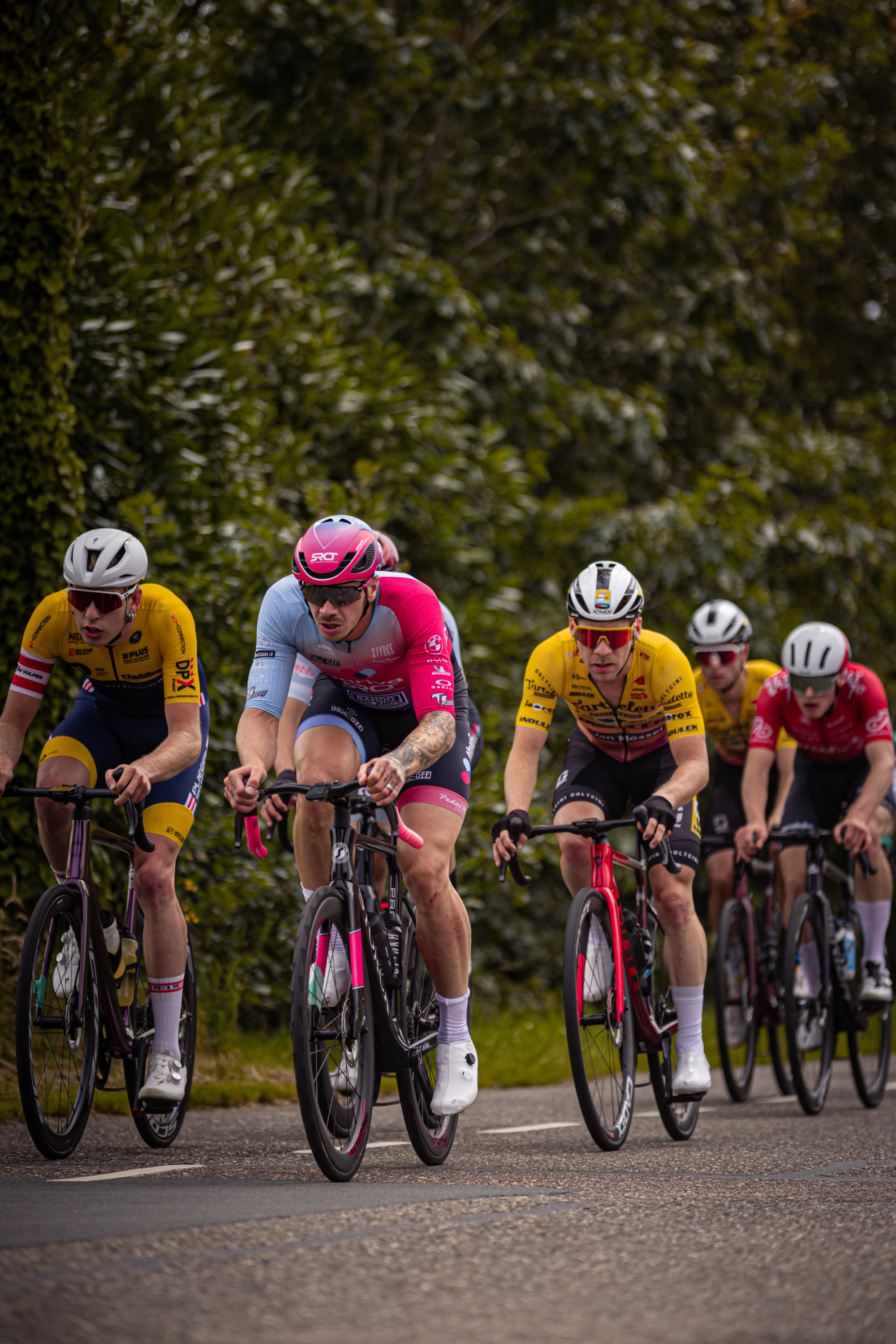 Five cyclists wearing helmets are racing in a group on a street. They have numbers 1, 2, and 4 on their jerseys.