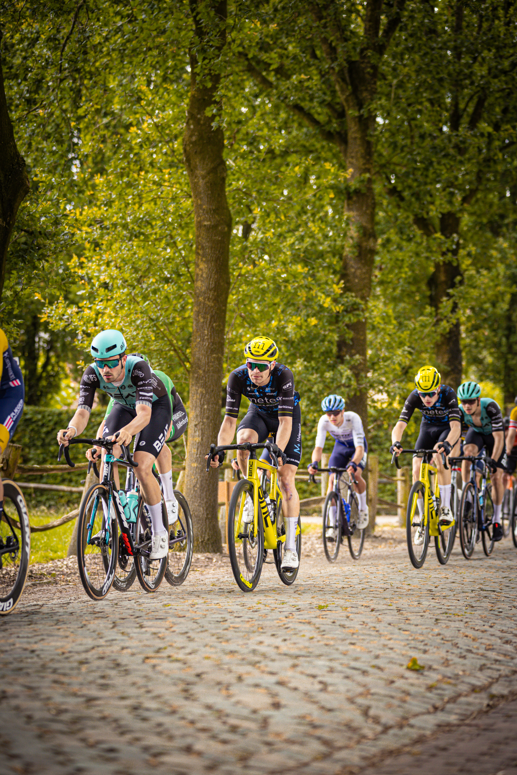 A group of cyclists riding through a park on a cobblestone path.