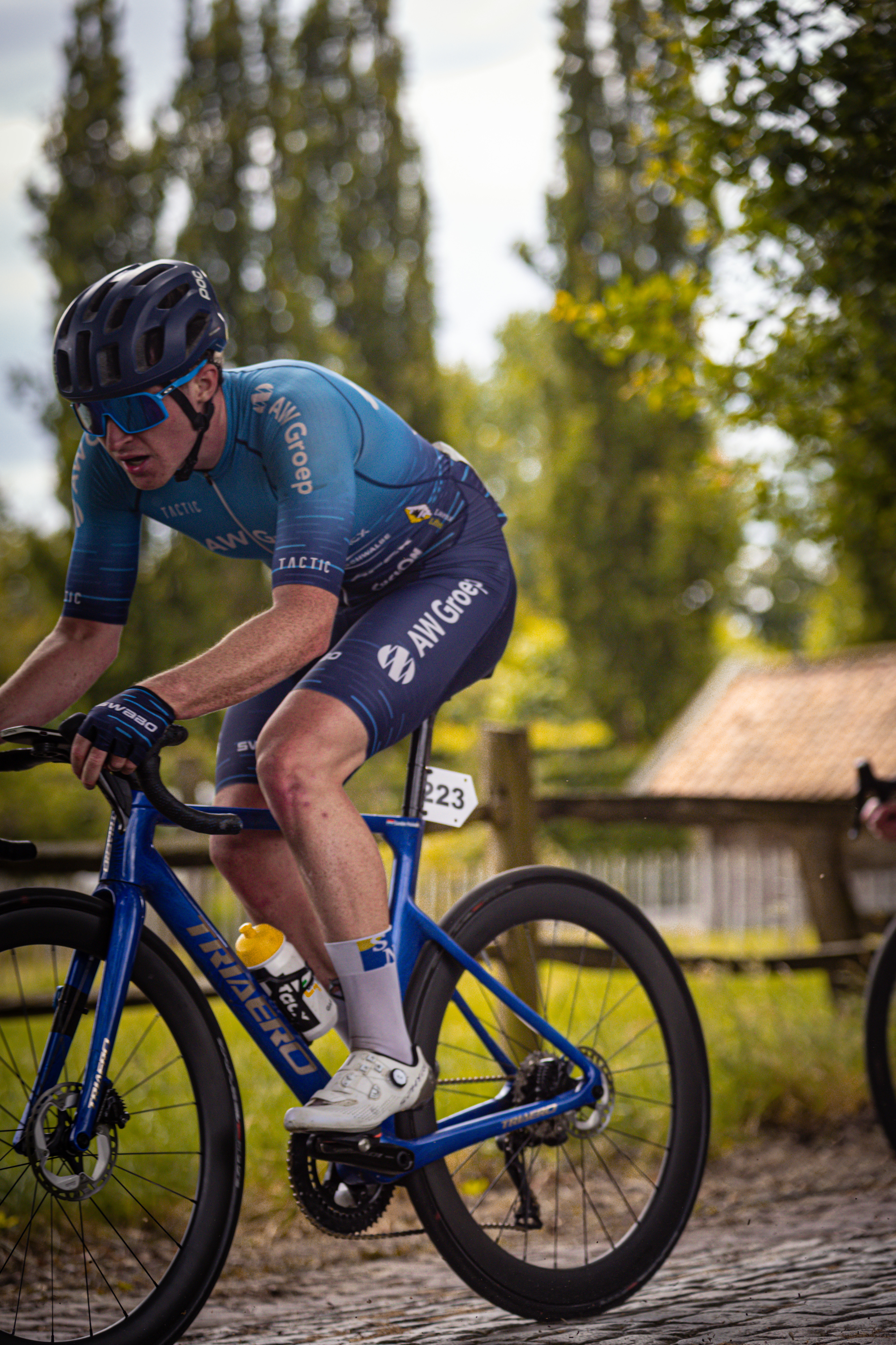 A blue cyclist racing in a race during the Midden Brabant Poort Omloop, sponsored by Wielrennen.