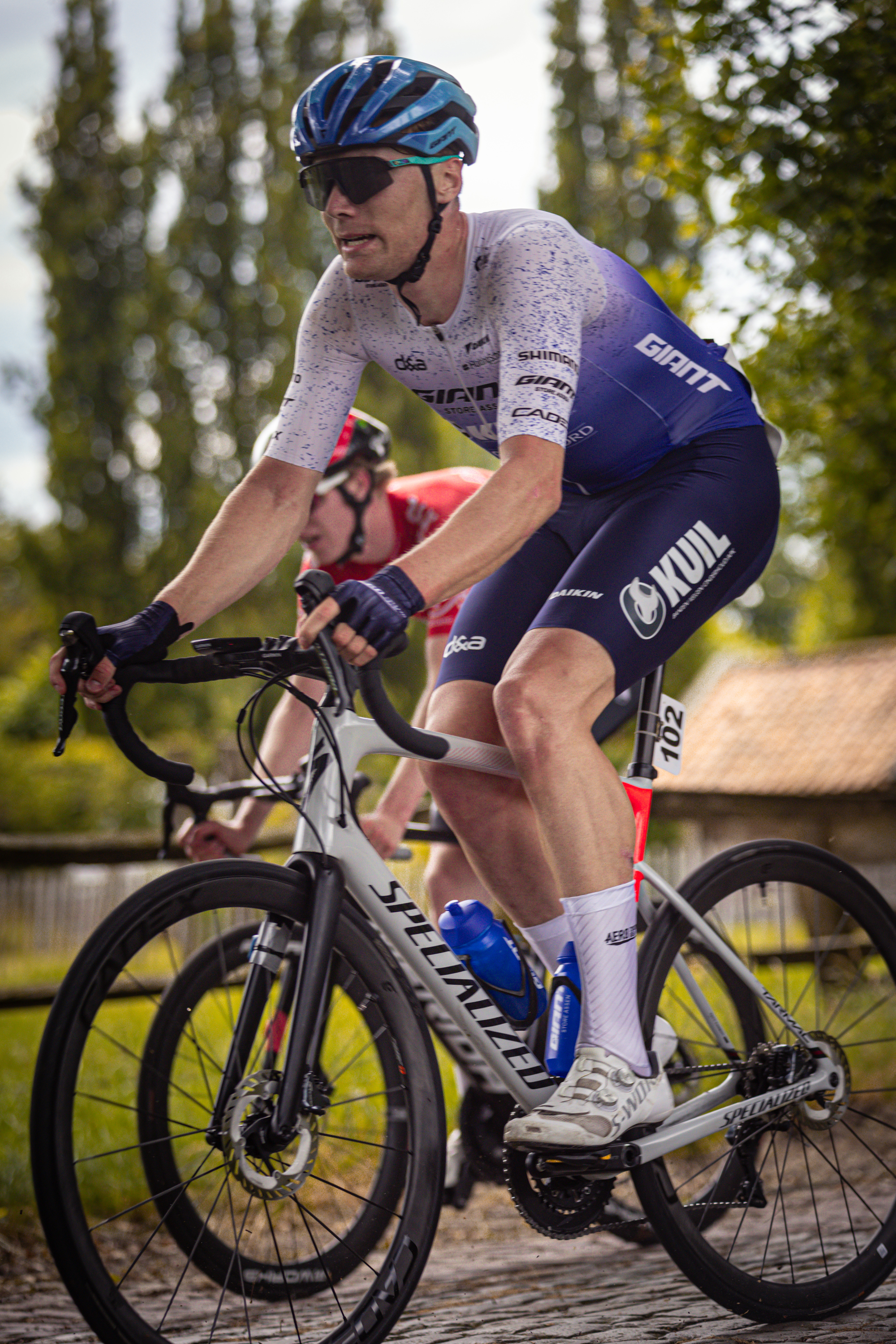 Two cyclists riding on a track with one wearing sunglasses.