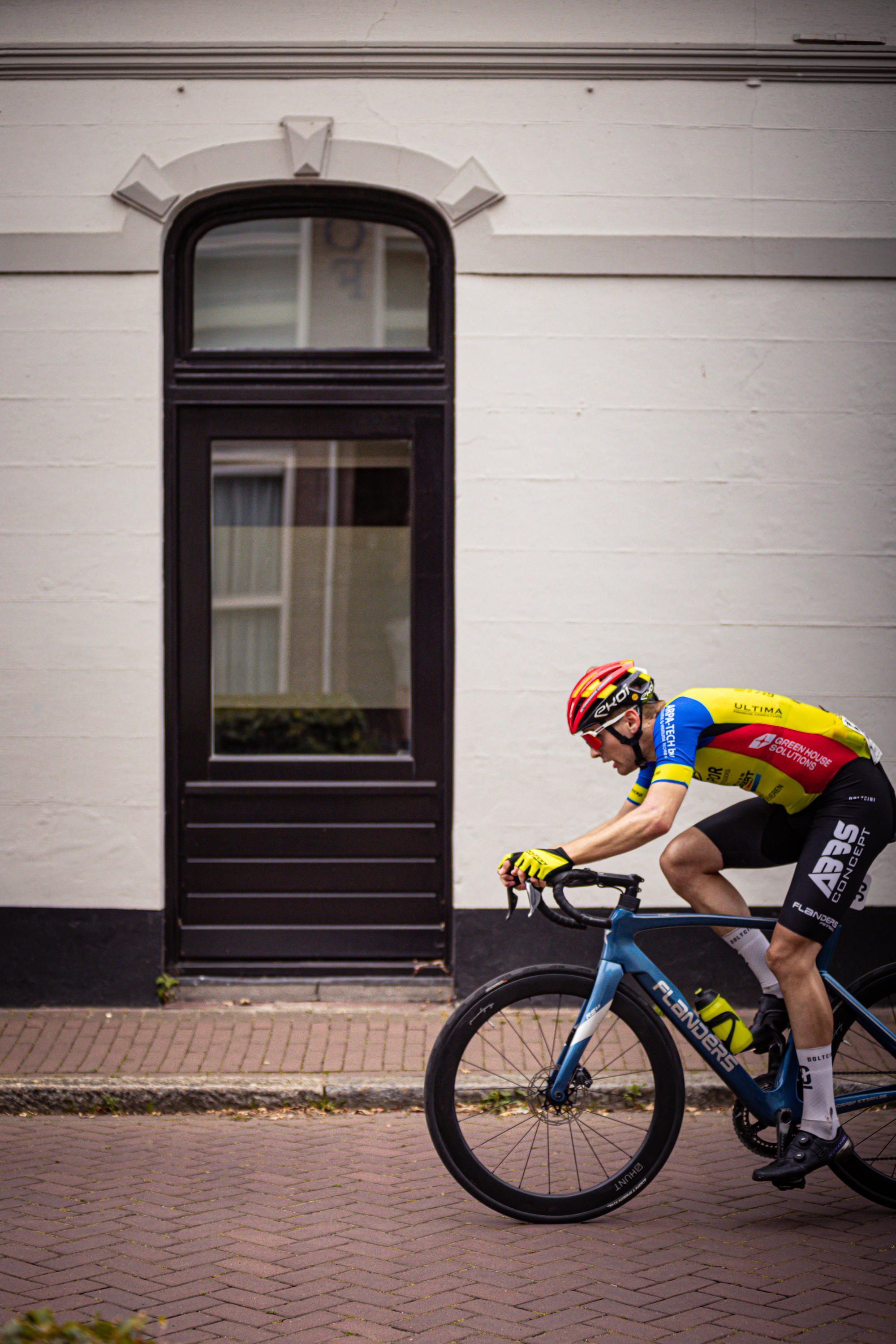 A man in a yellow and blue shirt is riding a bike past a door.