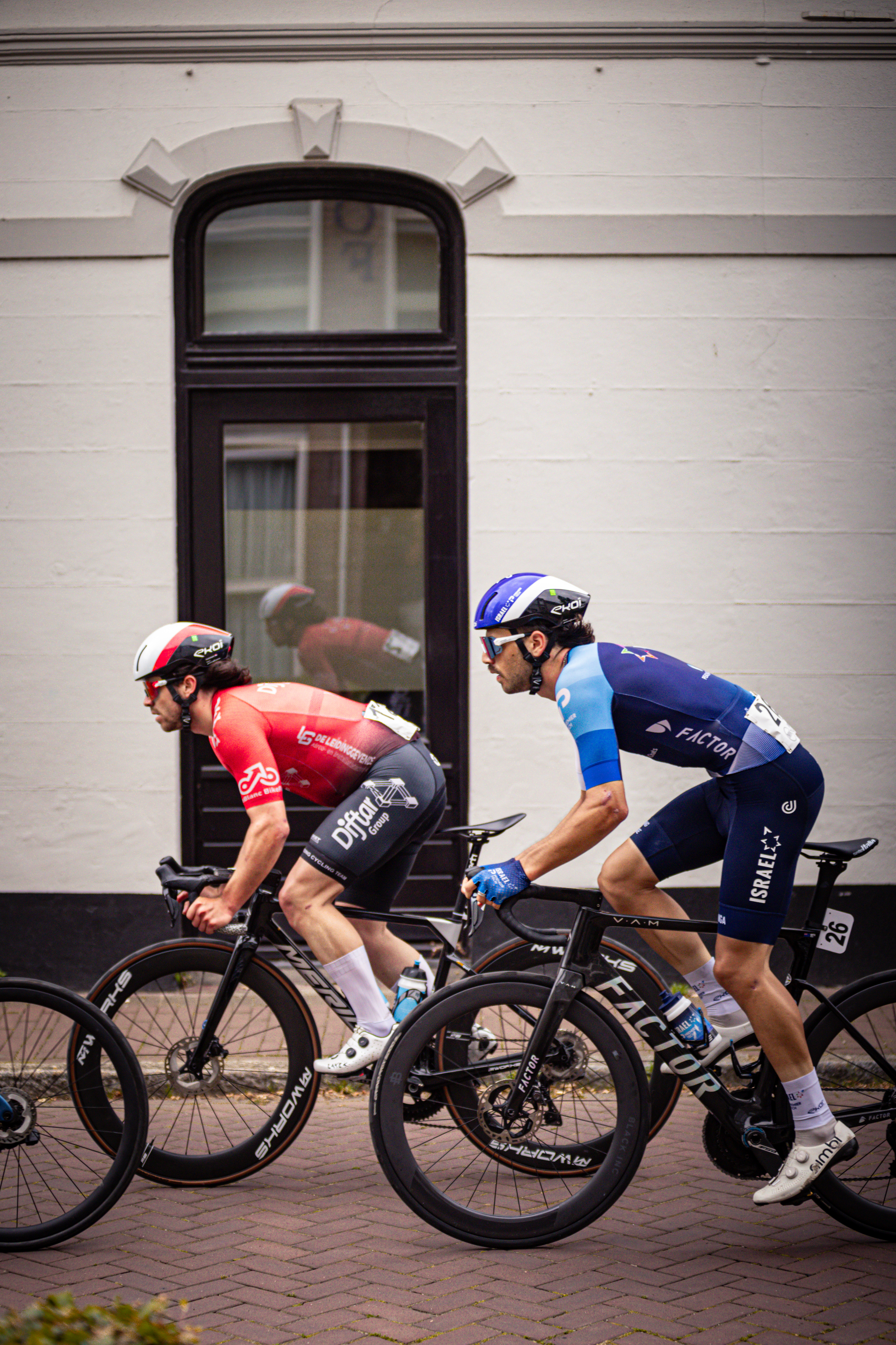 Three cyclist on road wearing a blue and red jersey and black bike.