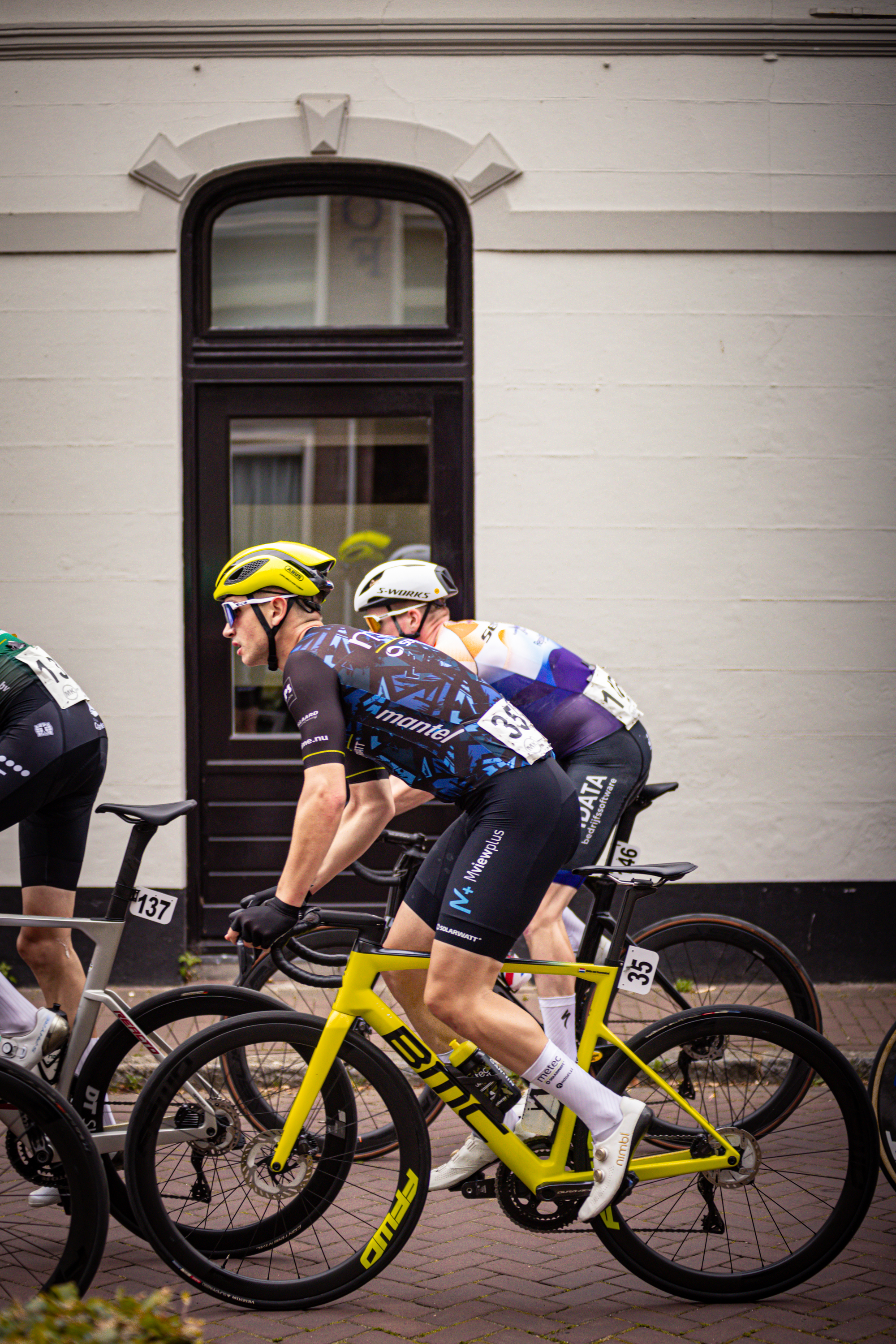 Three cyclists race past a building in the Midden Brabant Poort Omloop.