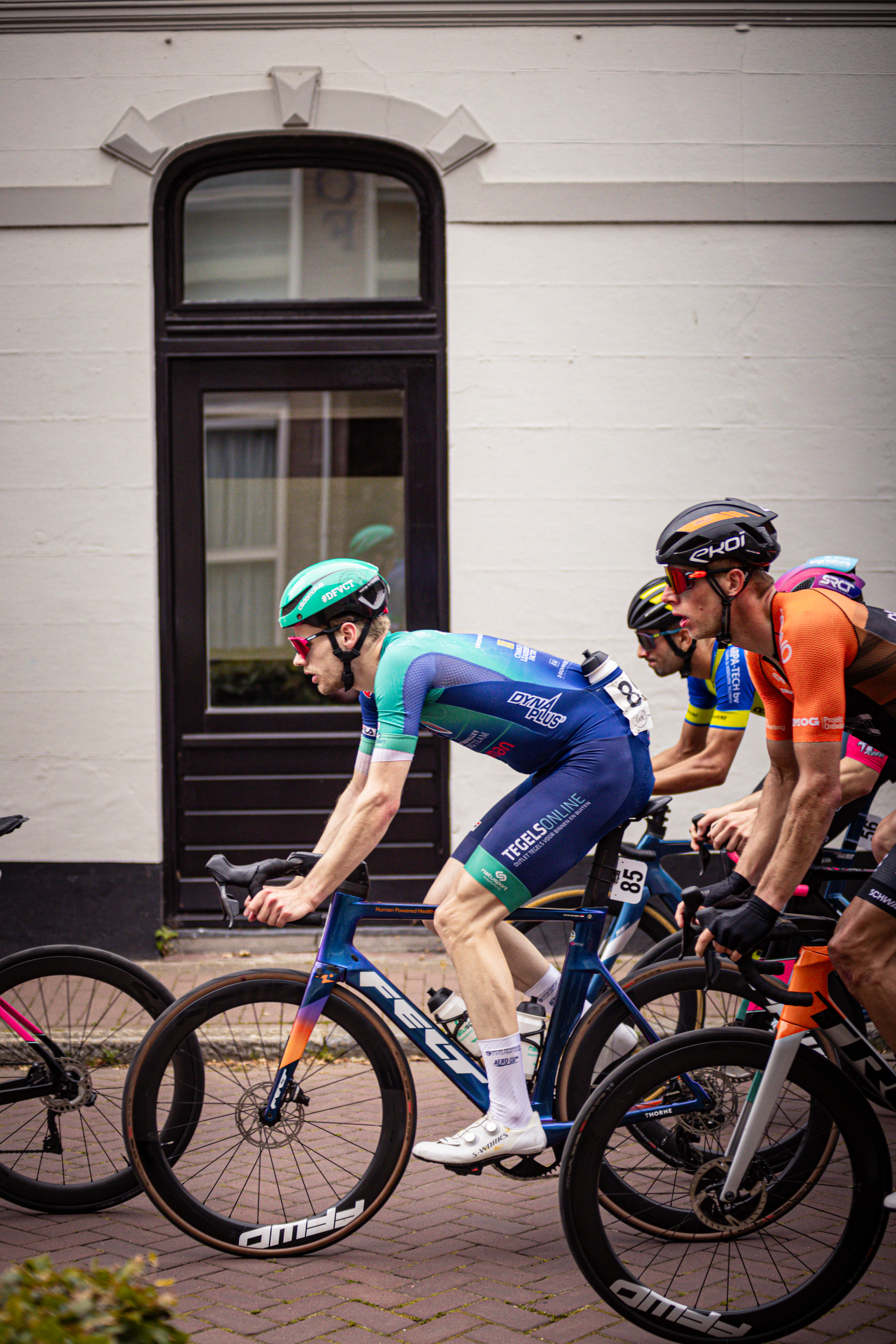 Several cyclists wearing helmets race down a street in front of an old building.