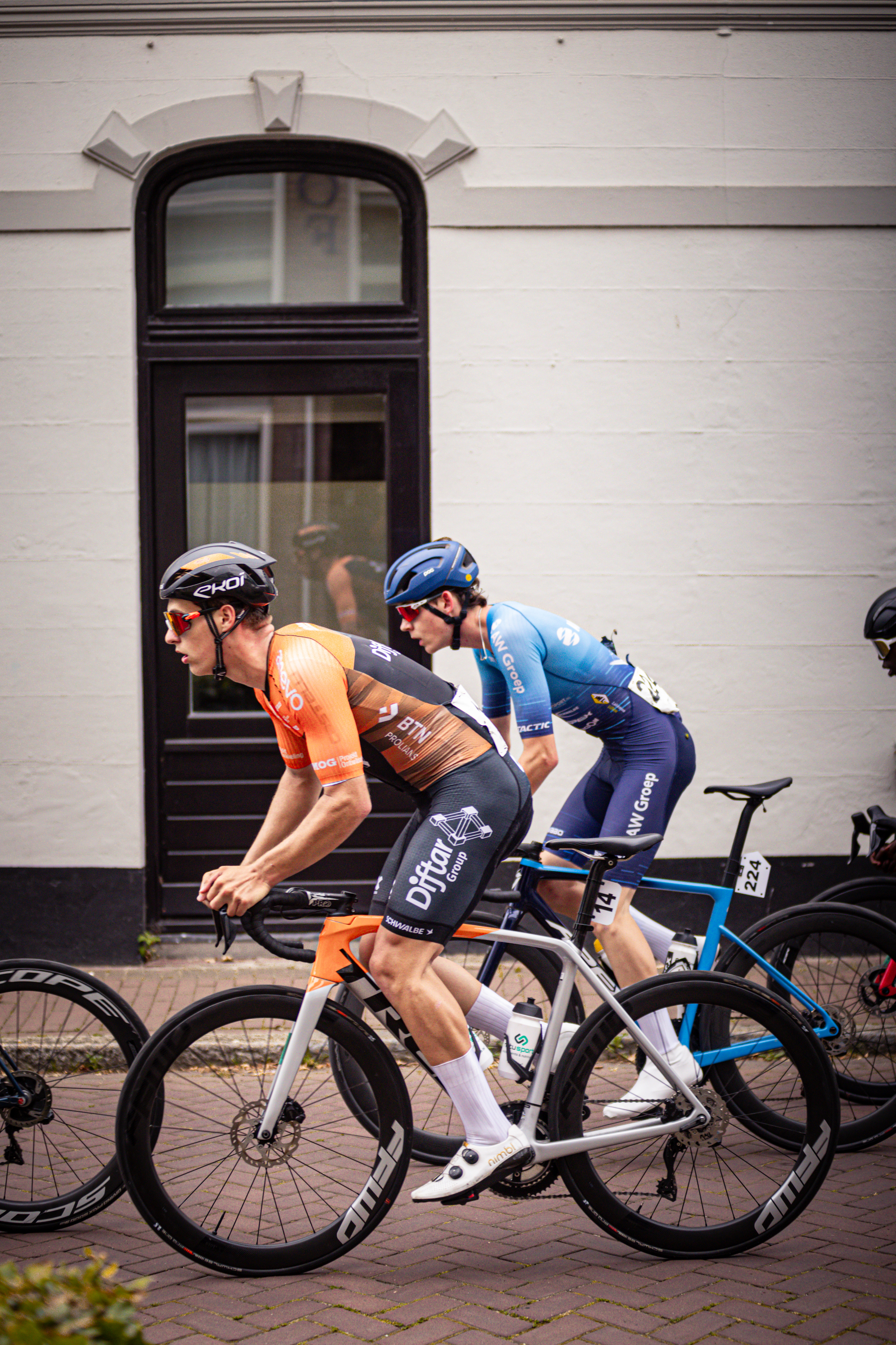 A group of cyclists wearing Wielrennen uniforms and helmets are riding their bikes.